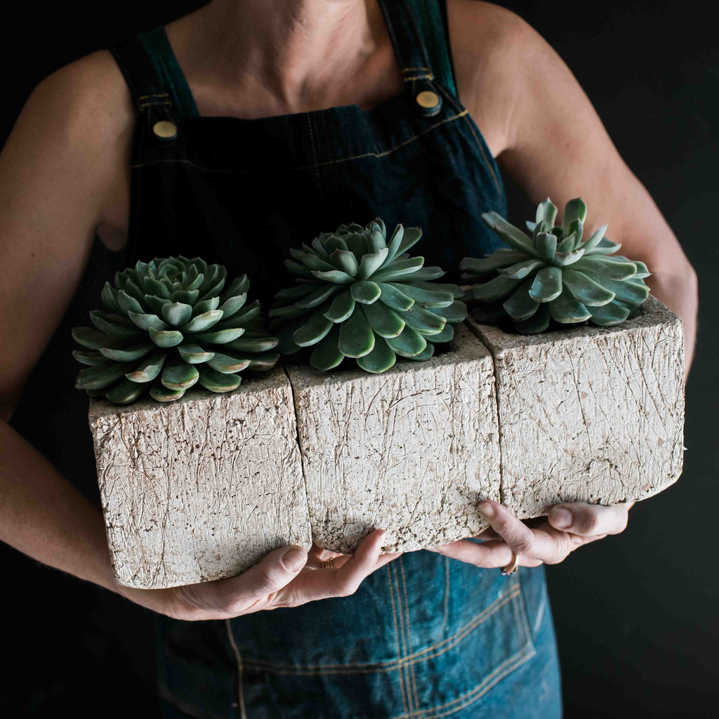 Made from our handmade Pozzola pottery.These bespoke living tablescapes come in a trio of our most popular mini cubes.   One modern organically shaped square, fits in the palm of both hands and has the feel and texture of washed stone but is ultra light weight. Each unique piece uses locally sourced drought tolerant succulents. This modern planter makes it easy to create a sustainable garden inside and out. It’s plant care made easy with drought tolerant living arrangements that last for years.